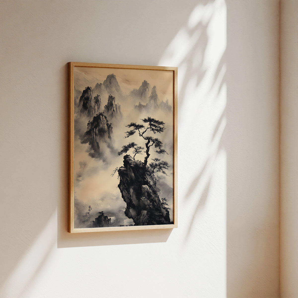 A framed vertical landscape painting of a pine tree on a rocky cliff surrounded by misty mountains, hanging on a warm beige wall with soft sunlight and leaf shadows.