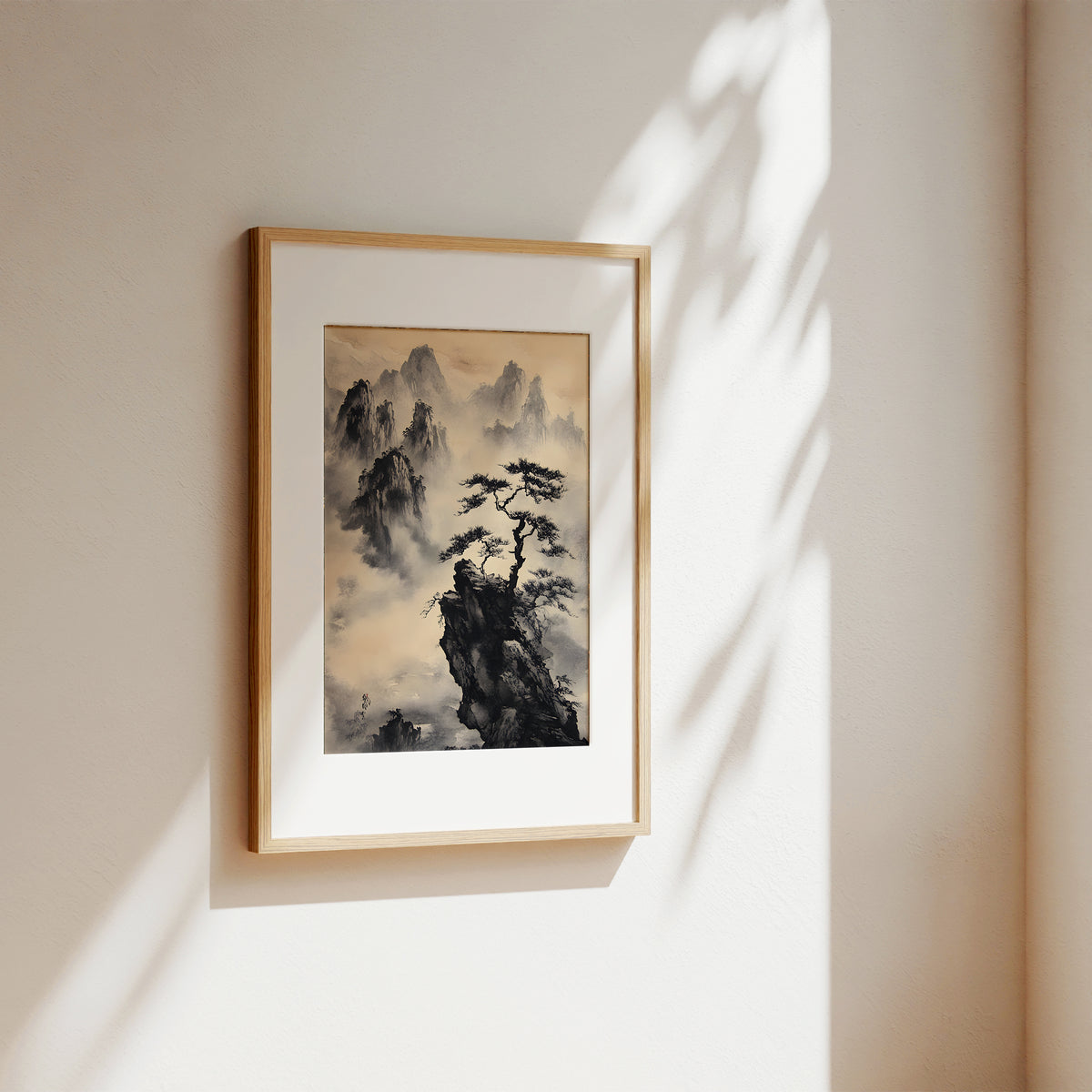 A framed vertical art print featuring a traditional black ink mountain landscape with mist and a lone pine tree, mounted on a warm beige wall with soft sunlight and leaf shadows.