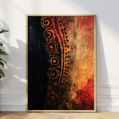 A framed vertical art print leaning against a white wall on a light wood floor, with a plant at the left edge. The artwork features a textured black-to-orange gradient with ornate circular and tribal-style patterns in dark brown tones, enclosed in a thin light wood frame.