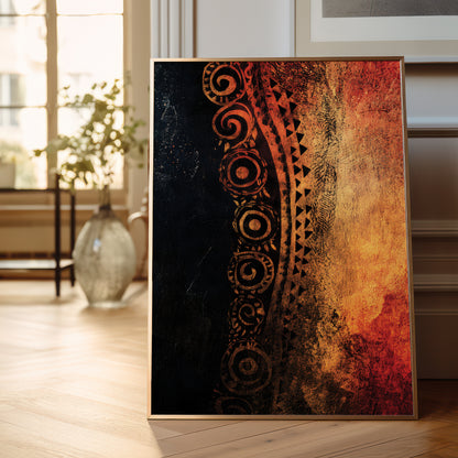 A framed vertical art print leaning against a wall on a light wood floor in a bright, modern room. The artwork features a textured design split diagonally, with a dark black-and-brown tribal pattern on the left and a warm orange, gold, and red abstract texture on the right.