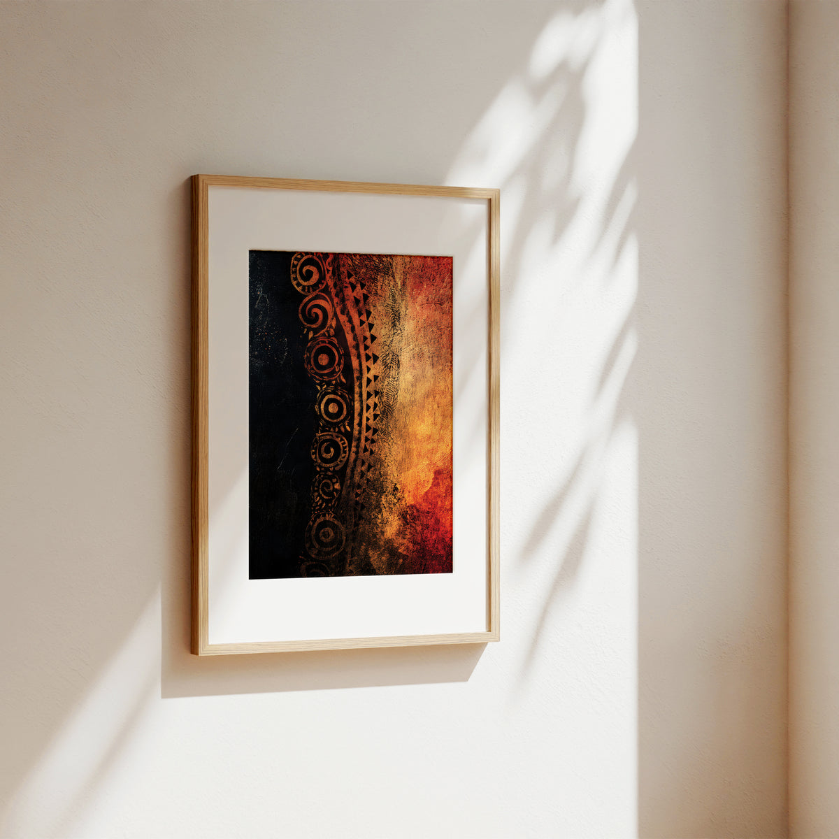Framed abstract wall art hanging on a warm off-white wall, with sunlight casting leaf shadows across the surface. The artwork features a vertical composition with a black textured left side, ornate gold circular motifs, and a fiery red, orange, and brown right side.