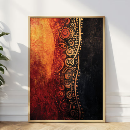 Framed abstract wall art leaning against a white wall on a light wood floor, with a plant partially visible at the left edge. The artwork features a vertical composition with fiery orange and red textures on the left, a black textured right side, and a central band of gold circular dot patterns.