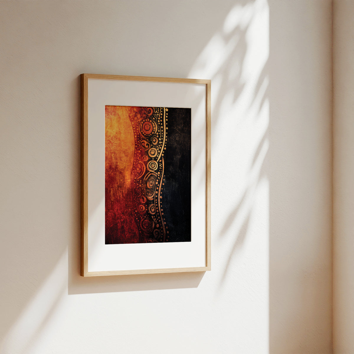 A framed abstract art print hanging on a warm beige wall, featuring a split design of fiery orange and red on one side and black with gold circular patterns on the other, framed in light wood with a white mat.