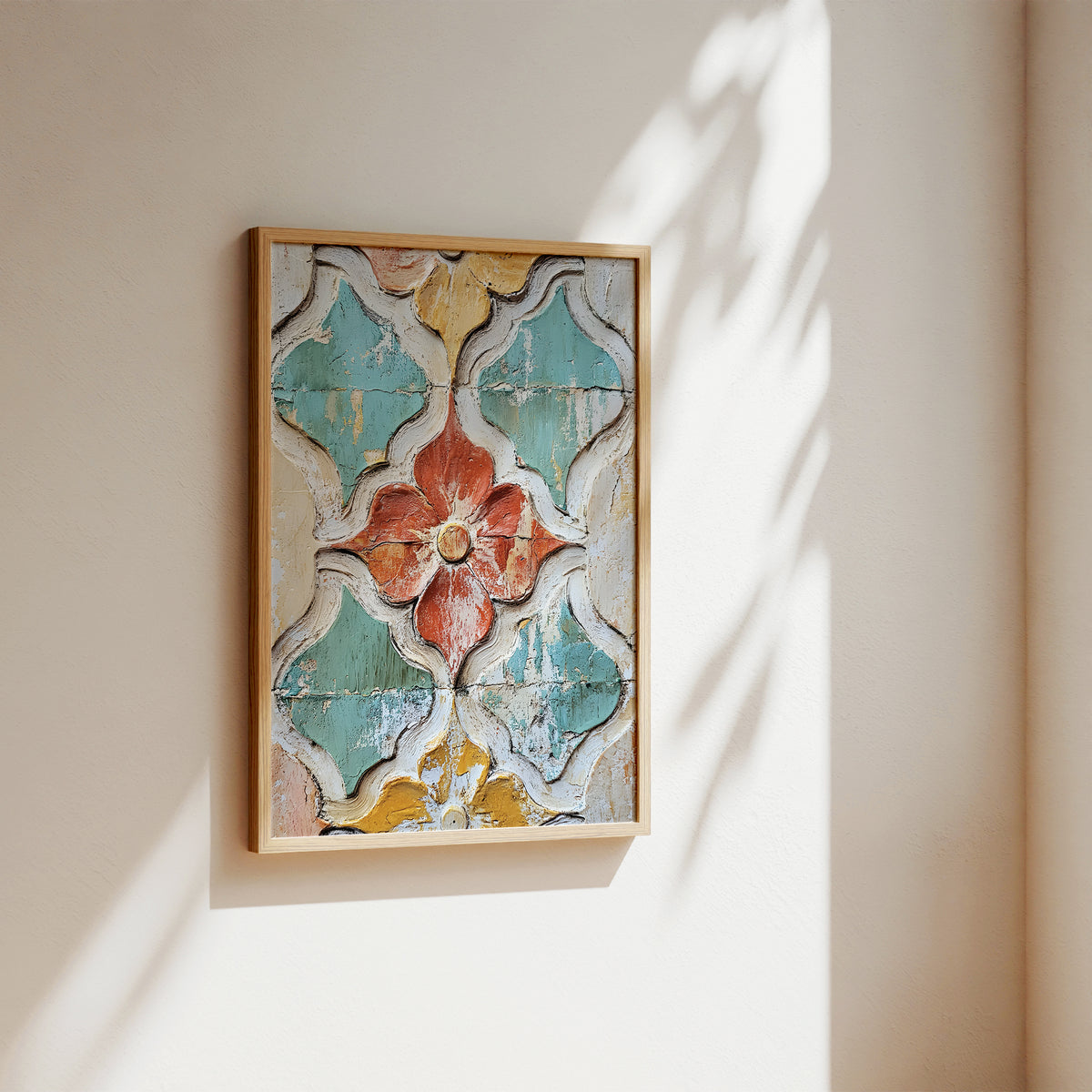 A framed decorative wall art piece hanging on a beige wall, featuring a distressed geometric floral pattern in muted teal, terracotta, cream, and ochre tones. Sunlight casts soft shadows across the wall and frame.