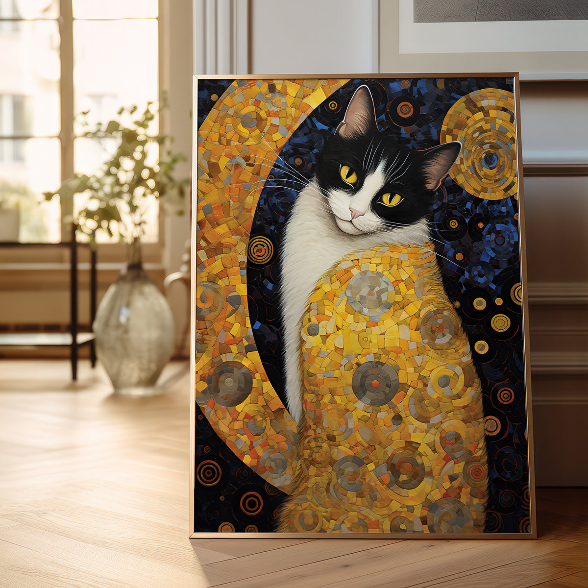 A framed vertical art print depicting a black and white cat in a stylized, textured golden-yellow and dark blue composition, leaning against a wall on a light wood floor in a softly lit room.