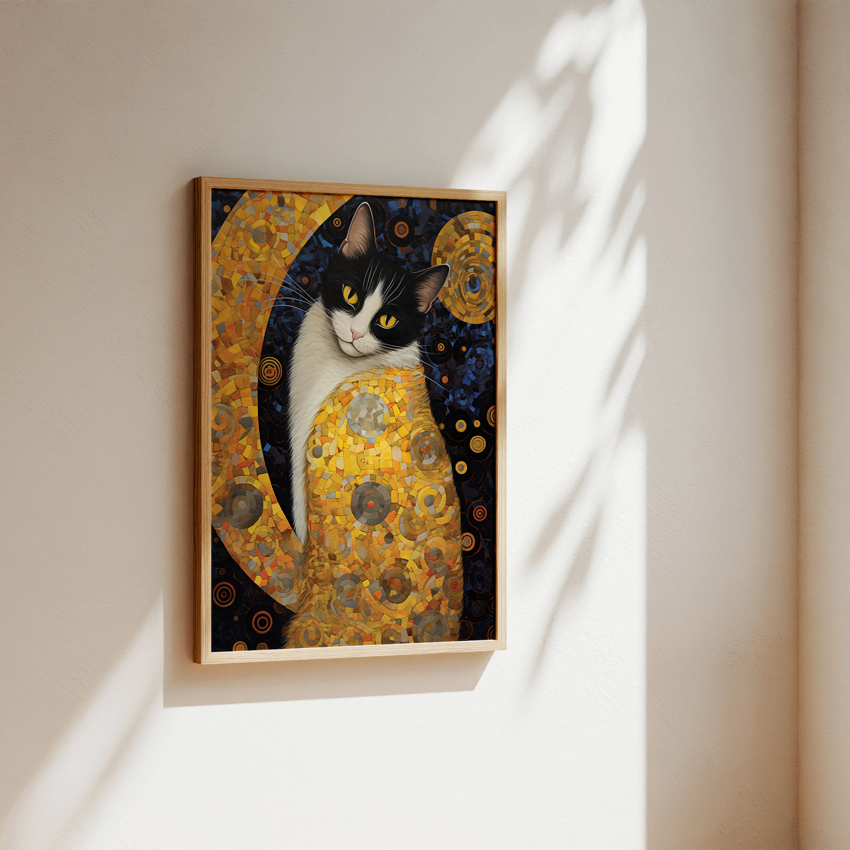 A framed art print of a black and white cat painted in a Gustav Klimt style with gold, yellow, and dark blue tones, hanging on a beige wall with soft sunlight and leaf shadows.