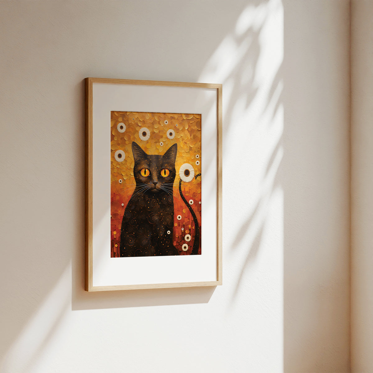 A framed art print featuring a black cat with glowing yellow eyes against a warm orange and gold background, hanging on a beige wall with soft sunlight and leaf shadows.