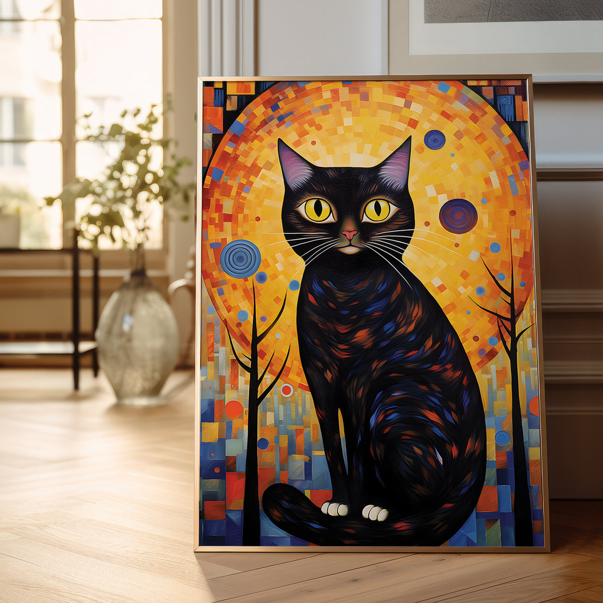A framed vertical art print depicting a black cat with yellow eyes against a colorful mosaic sun and trees, leaning against a wall on a light wood floor in a bright room.