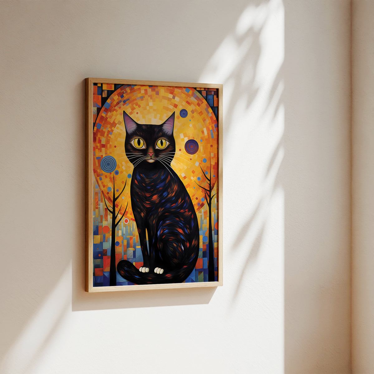 A framed art print of a stylized black cat with yellow eyes against a warm orange and blue mosaic background, hanging on a beige wall with soft sunlight and leaf shadows.