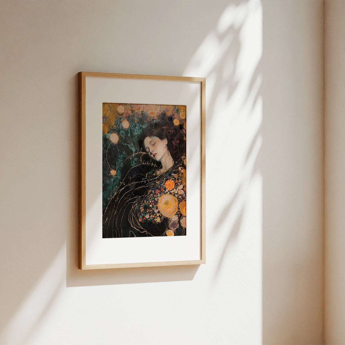 A framed art print featuring a stylized portrait of a woman with dark hair and orange floral elements, displayed on a warm beige wall with soft sunlight and leaf shadows.