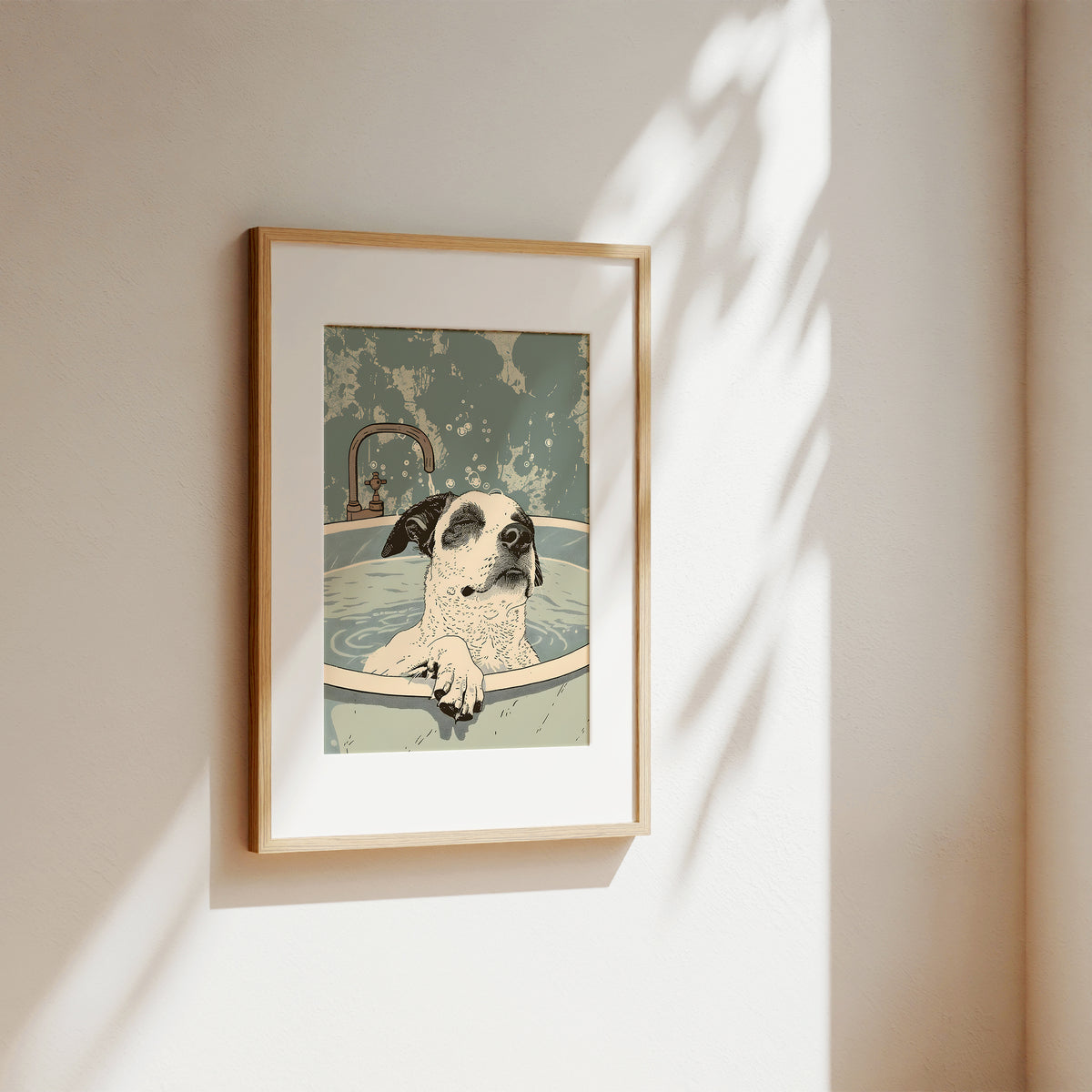 A framed art print featuring a dog sitting in a bathtub, hung on a beige wall with soft sunlight and leaf shadows casting across it.