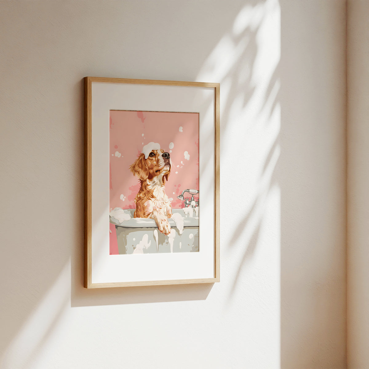 A framed art print featuring a cartoon dog in a pink bath scene, hung on a beige wall with soft sunlight and leaf shadows casting across it.