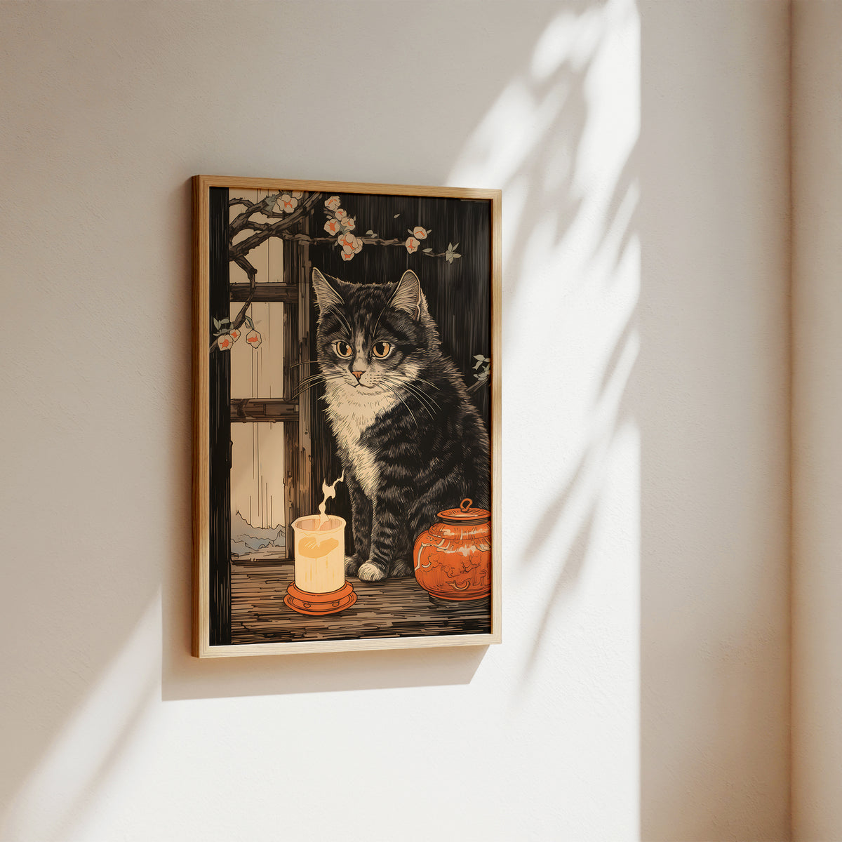 A framed art print featuring a tabby cat sitting beside a lit candle and an orange ceramic jar, hung on a warm beige wall with soft sunlight and leaf shadows cast across it.