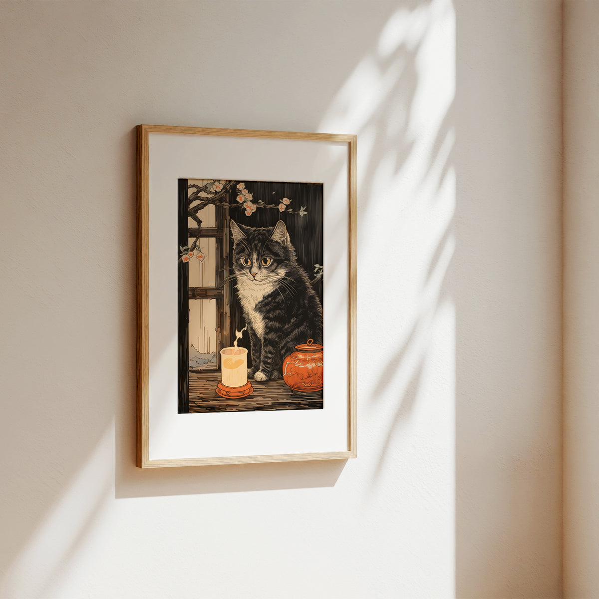 A framed art print featuring a tabby cat sitting beside a candle and a small orange pumpkin, hung on a warm beige wall with soft sunlight and leaf shadows cast across it.