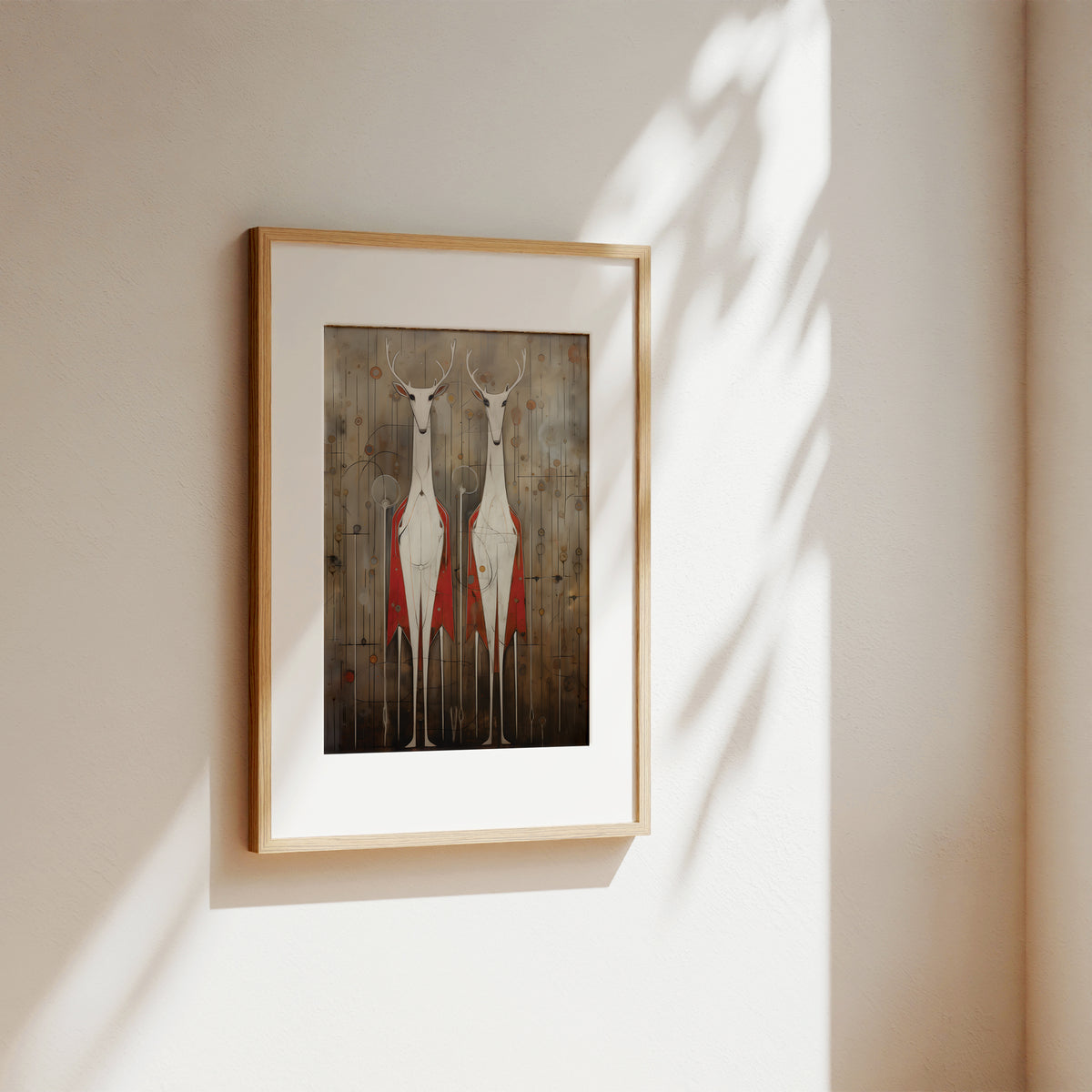 A framed art print featuring two stylized red and white deer against a rustic wood background, displayed on a warm beige wall with soft sunlight and leaf shadows.