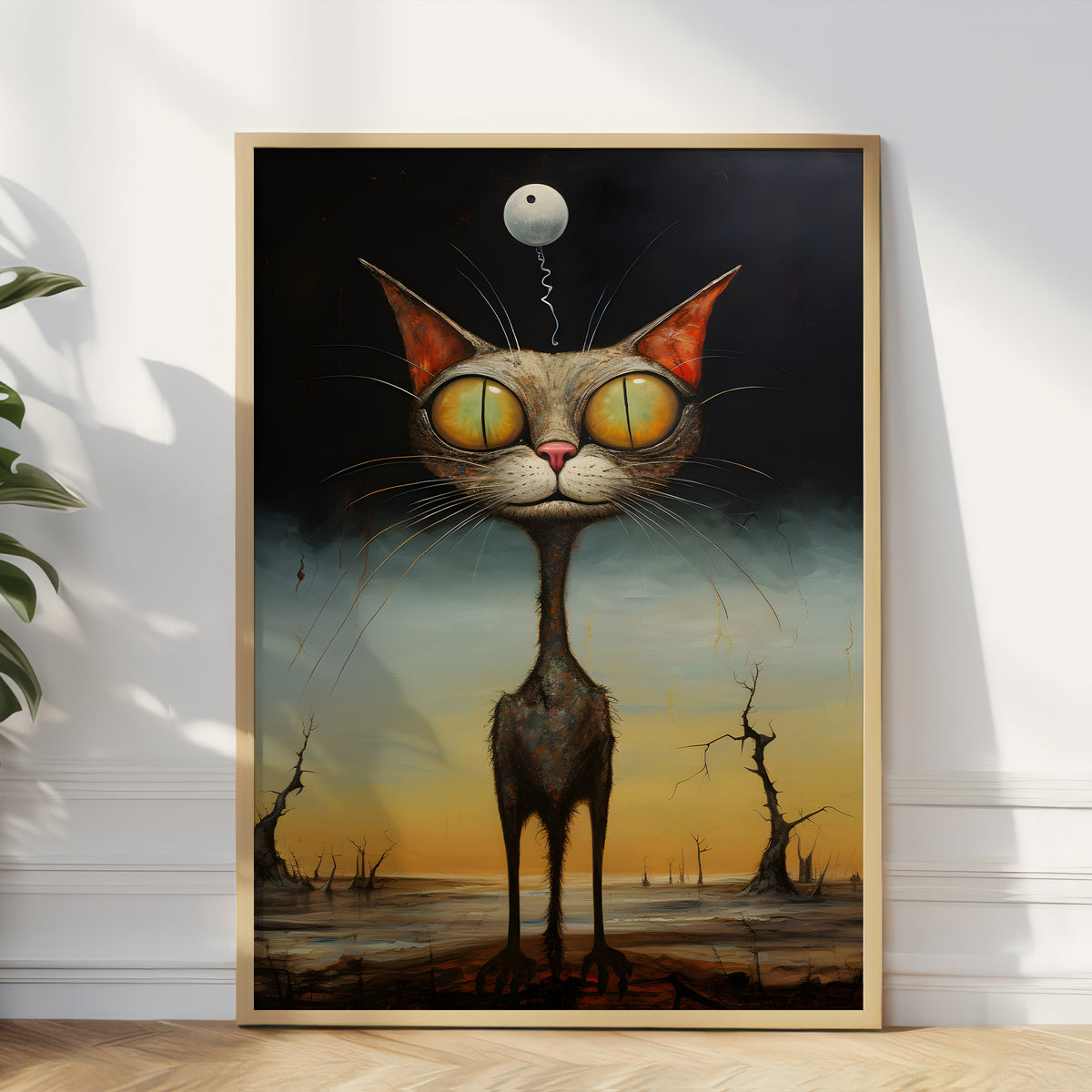 A framed surreal art print leaning against a white wall on a light wood floor, showing a tall gray cat with oversized yellow eyes and a small moon floating above its head in a dark, moody landscape.