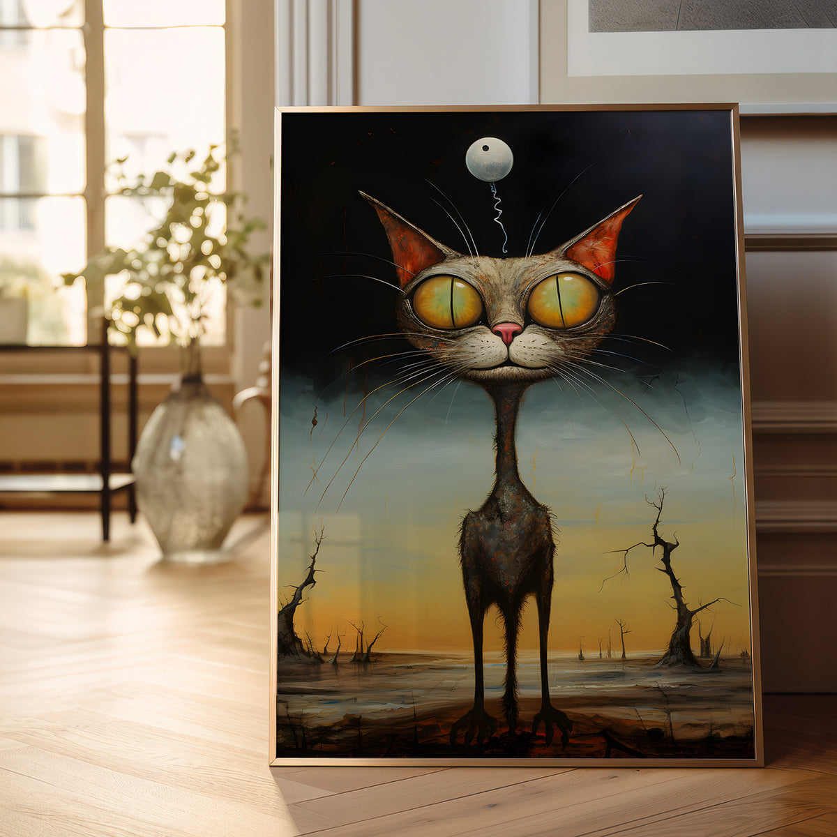 A framed surreal art print leaning against a wall on a wooden floor, showing a tall gray cat with oversized yellow eyes and a small floating moon above its head, set in a softly lit interior with a vase and window in the background.