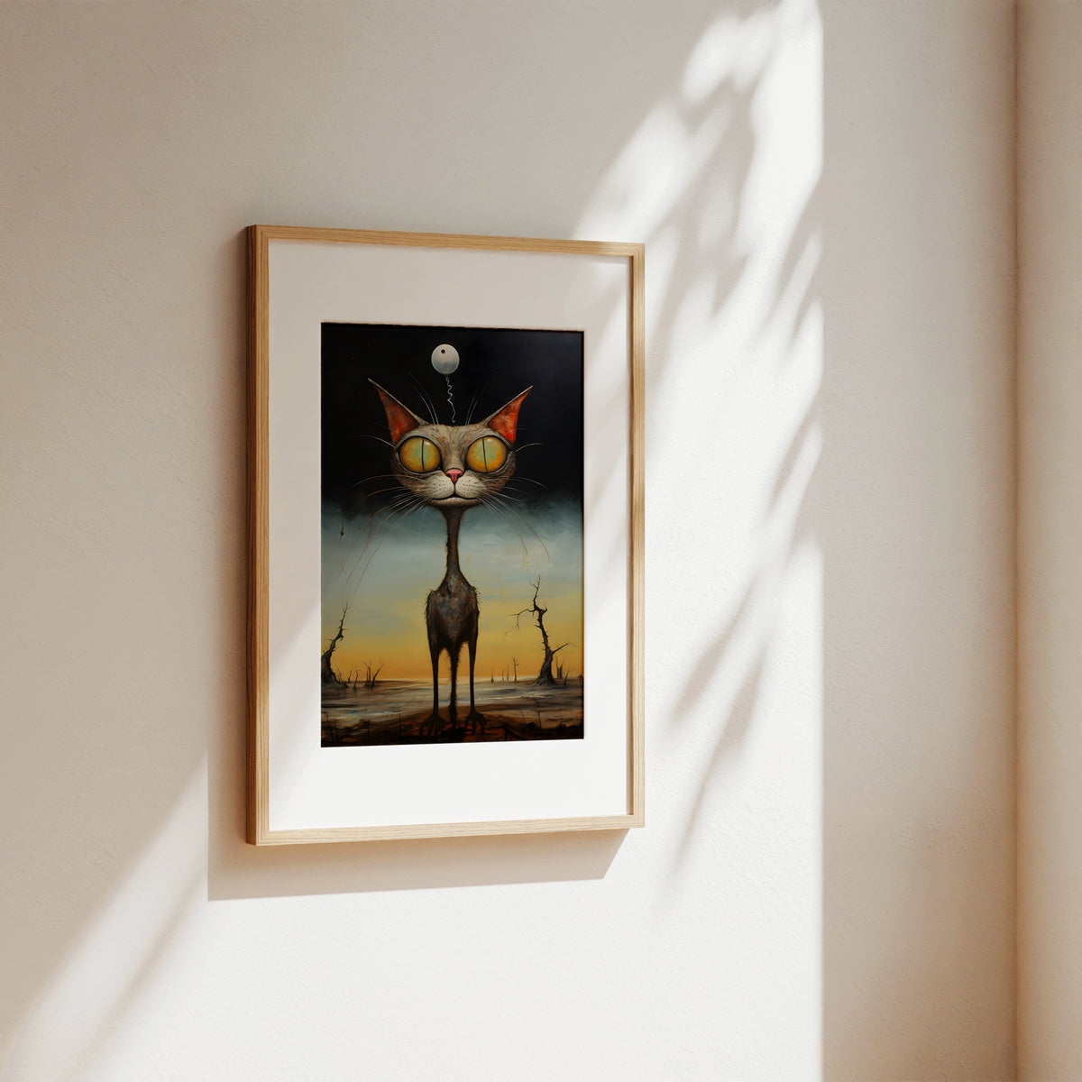 A framed surreal art print of a tall cat with yellow goggles and a moon on its head, displayed on a warm beige wall with soft window shadows.