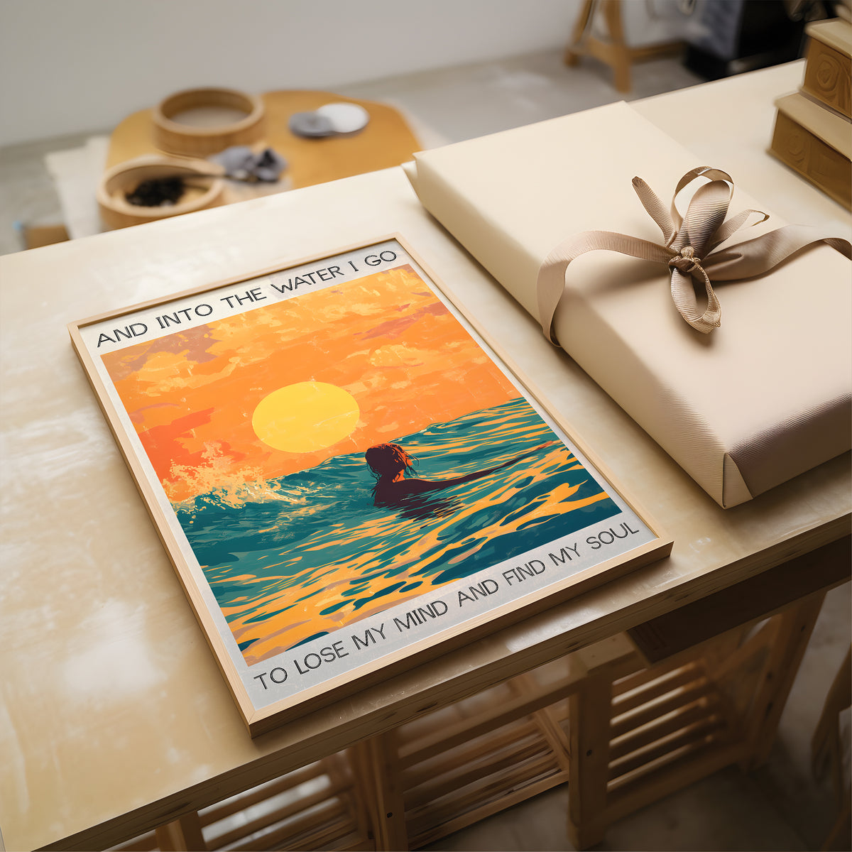 Poster of a person in water with a sunset and text, placed on a table next to a wrapped gift.