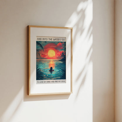 Framed artwork of a sunset over water with a person in the water, on a beige wall.