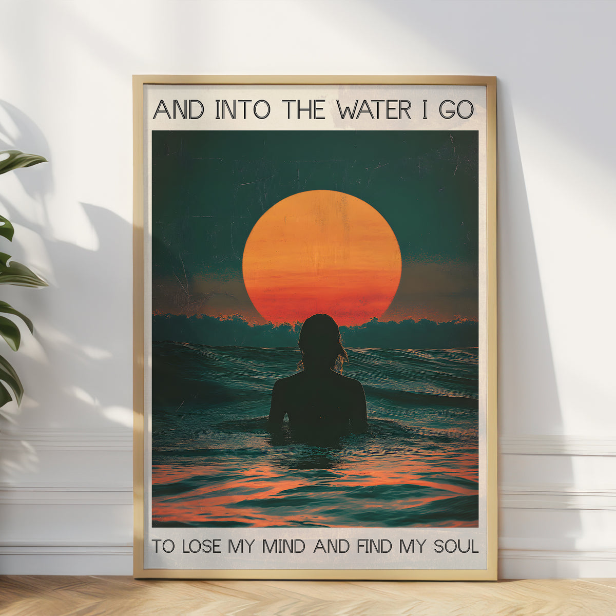 Framed artwork of a person in water with a sunset, text 'And into the water I go / To lose my mind and find my soul', on a white wall.