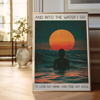 Framed poster of a sunset over water with a person in silhouette, placed on a wooden floor.