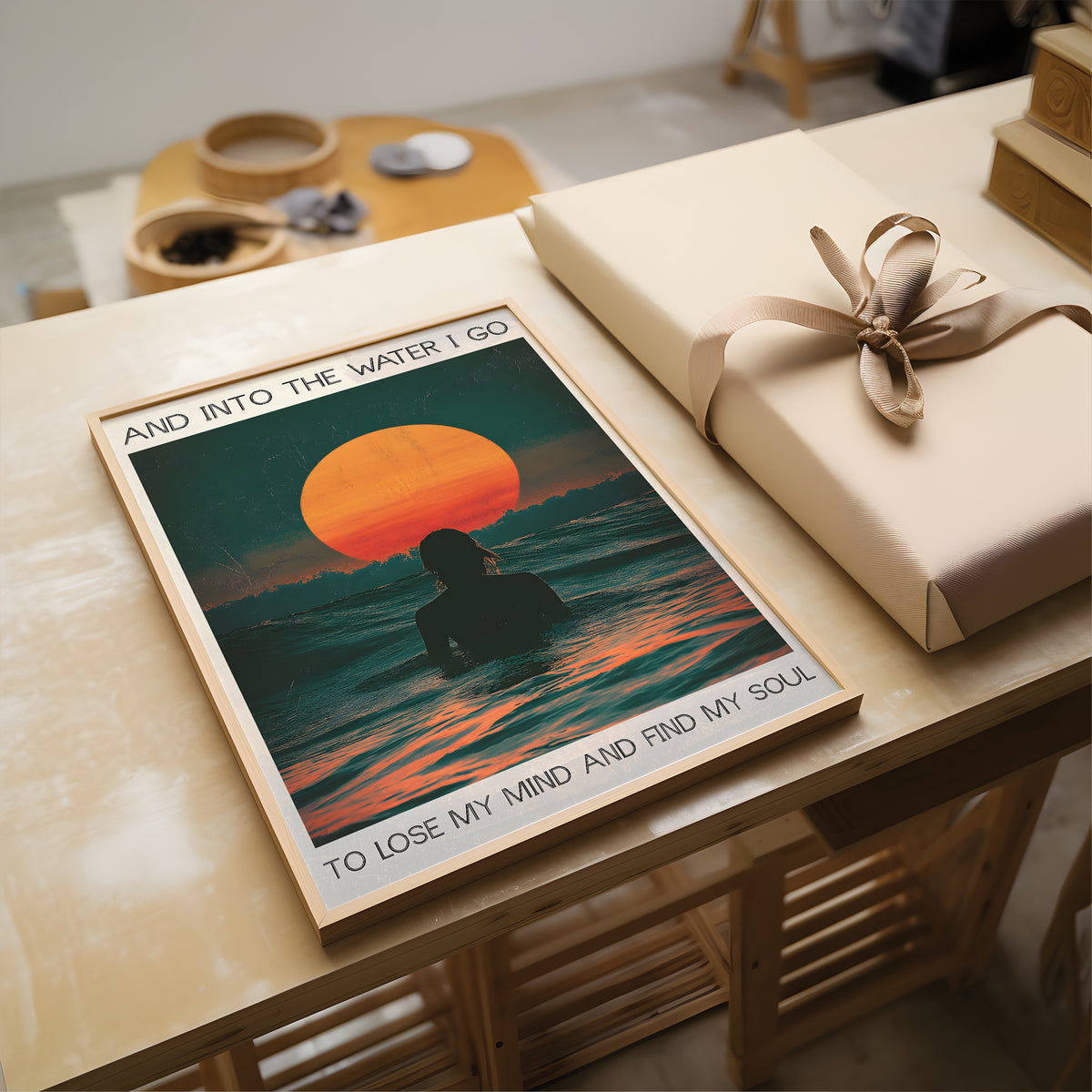 Poster of a sunset over water with a silhouette of a person, placed on a table next to a wrapped gift.