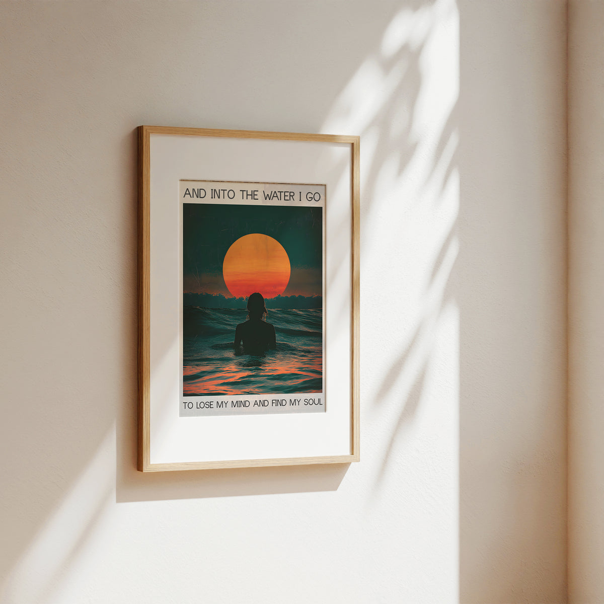 Framed artwork of a sunset over water with a person in the foreground, on a beige wall.
