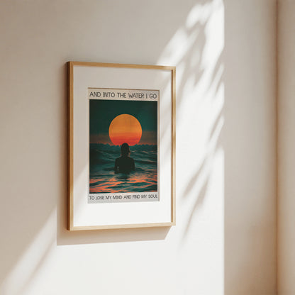 Framed artwork of a sunset over water with a person in the foreground, on a beige wall.