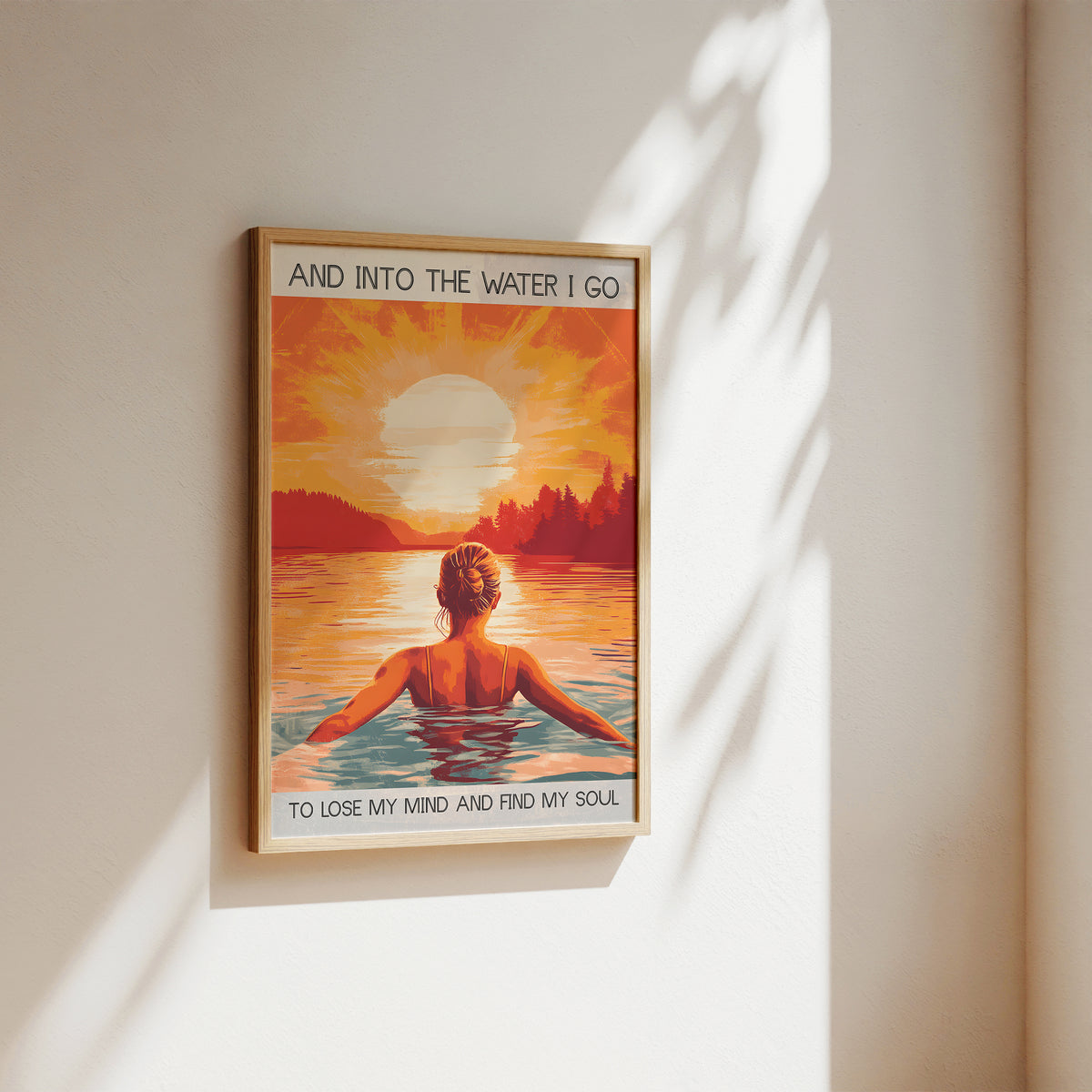 Framed artwork of a woman sitting by a lake with a sunset, text 'And into the water I go to lose my mind and find my soul'.