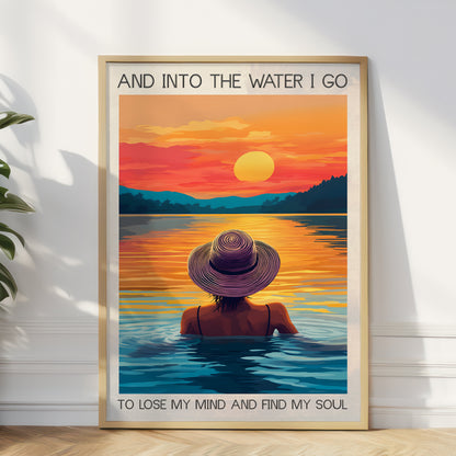 Framed artwork of a person in a hat sitting in water with a sunset over a lake.