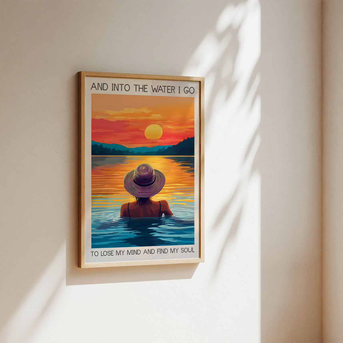 Framed artwork of a person in a hat sitting by water with a sunset, on a beige wall.
