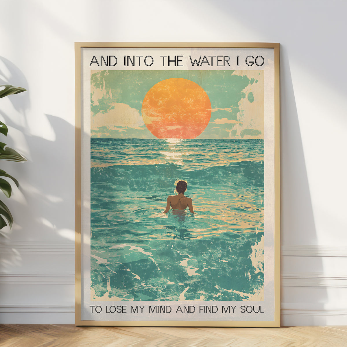 Framed artwork of a person in water with a sunset, text 'And into the water I go / To lose my mind and find my soul', on a white wall.