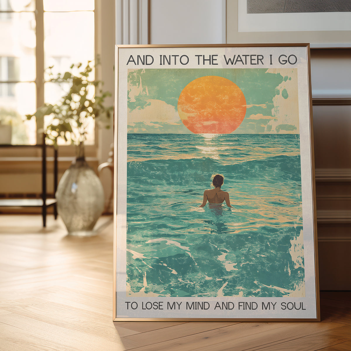 Framed poster of a person in the water with a sunset, placed on a wooden floor.