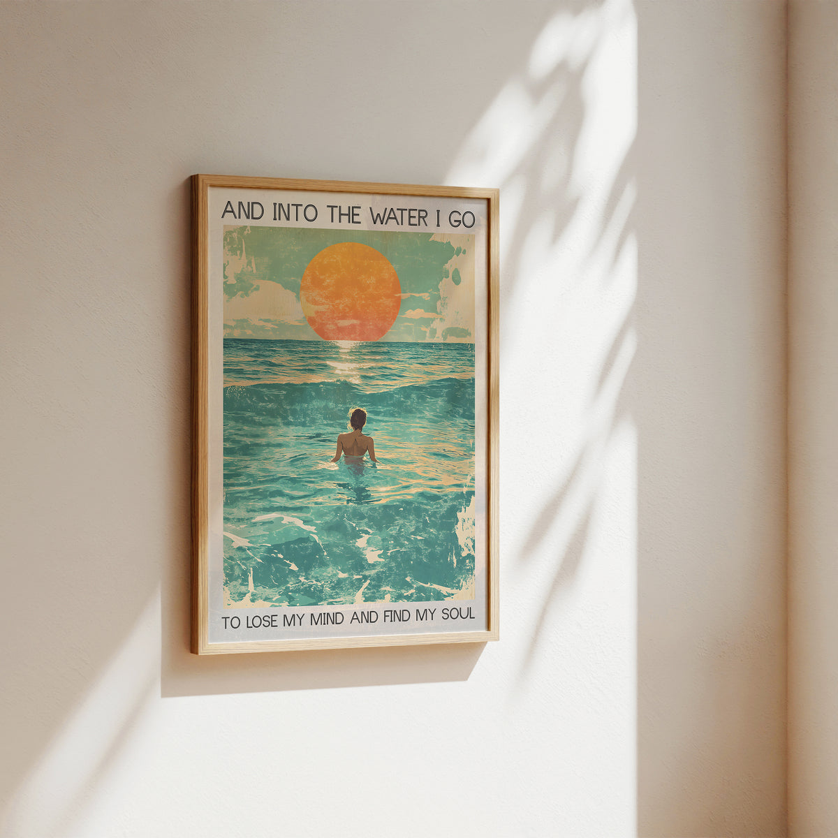 Framed artwork of a person in the water with a sunset, on a beige wall.