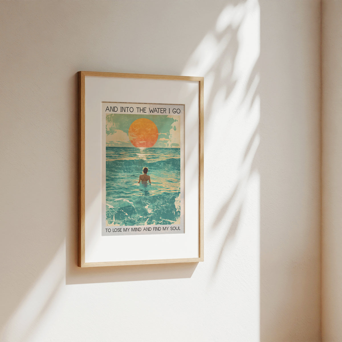 Framed artwork of a person in the ocean with a sunset, on a beige wall.