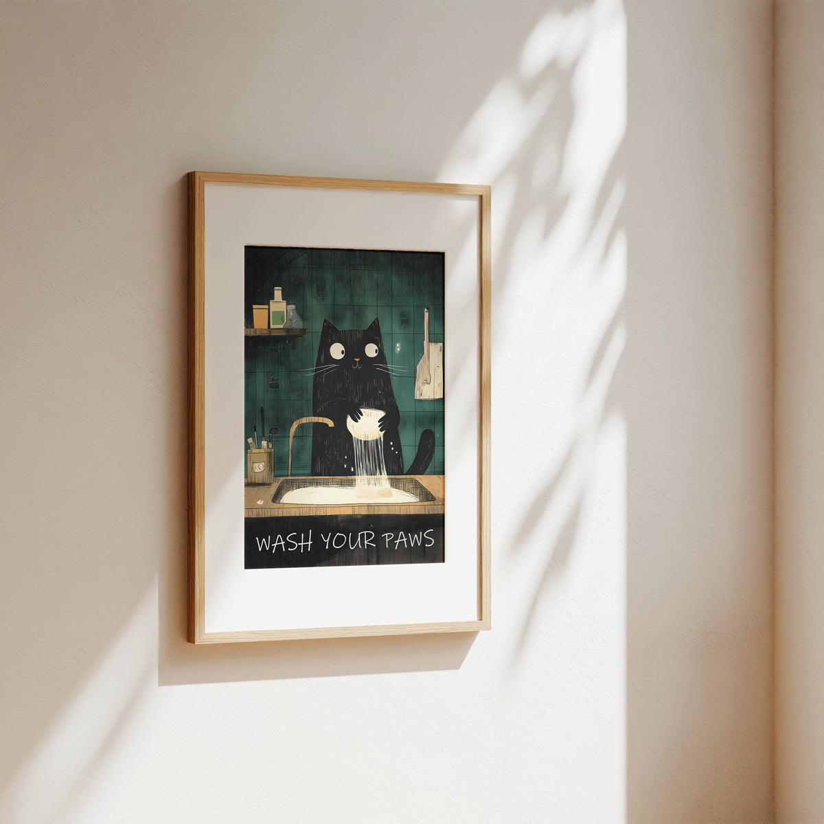 A framed art print featuring a black cat washing its paws at a sink, hung on a beige wall with soft sunlight and leaf shadows cast across it.