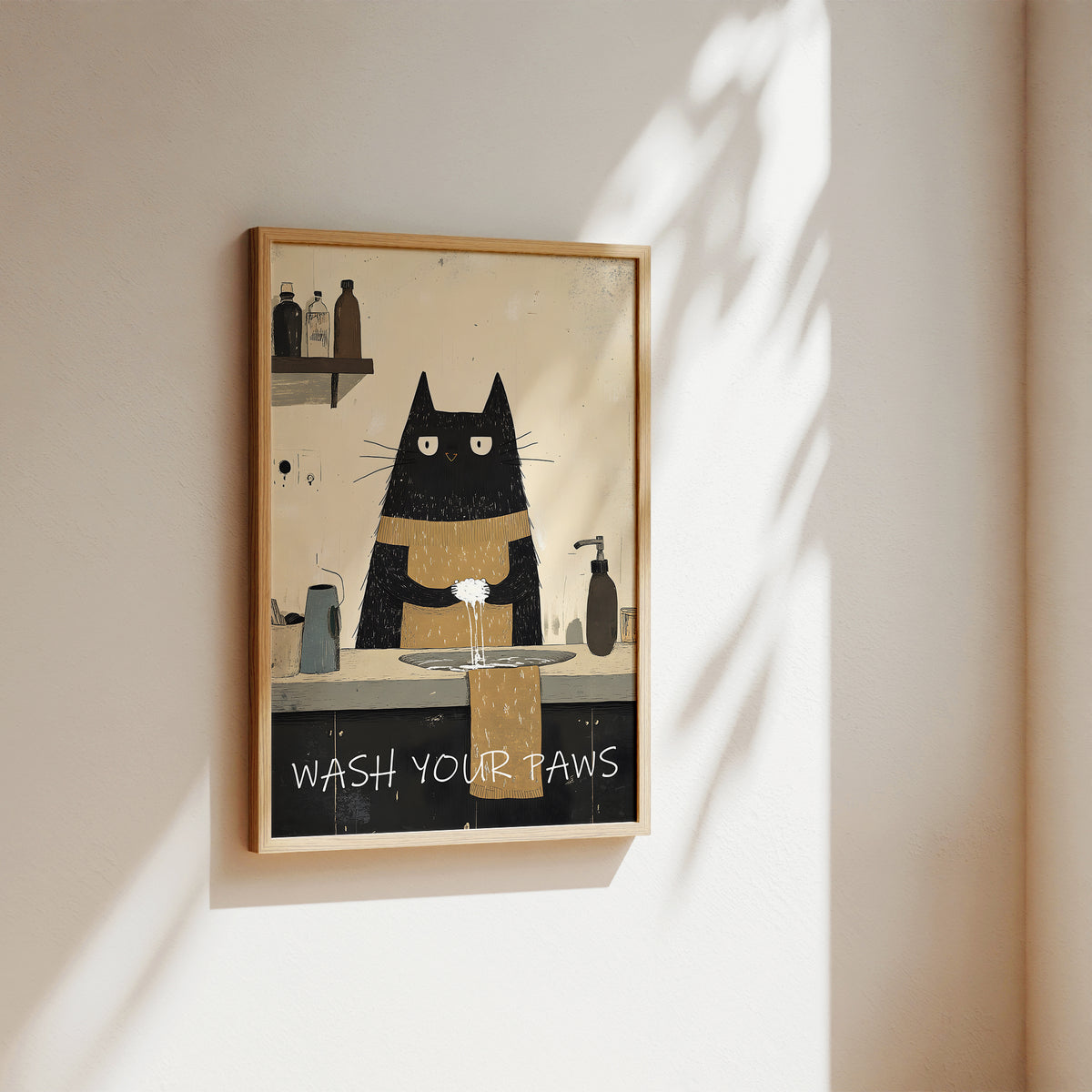 A framed art print featuring a minimalist black cat with a gold collar washing its paws at a sink, hanging on a warm beige wall with soft sunlight and leaf shadows.