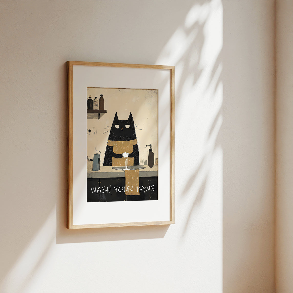 A framed art print featuring a black cat with white paws washing its teeth, hung on a warm beige wall with soft leaf shadows.
