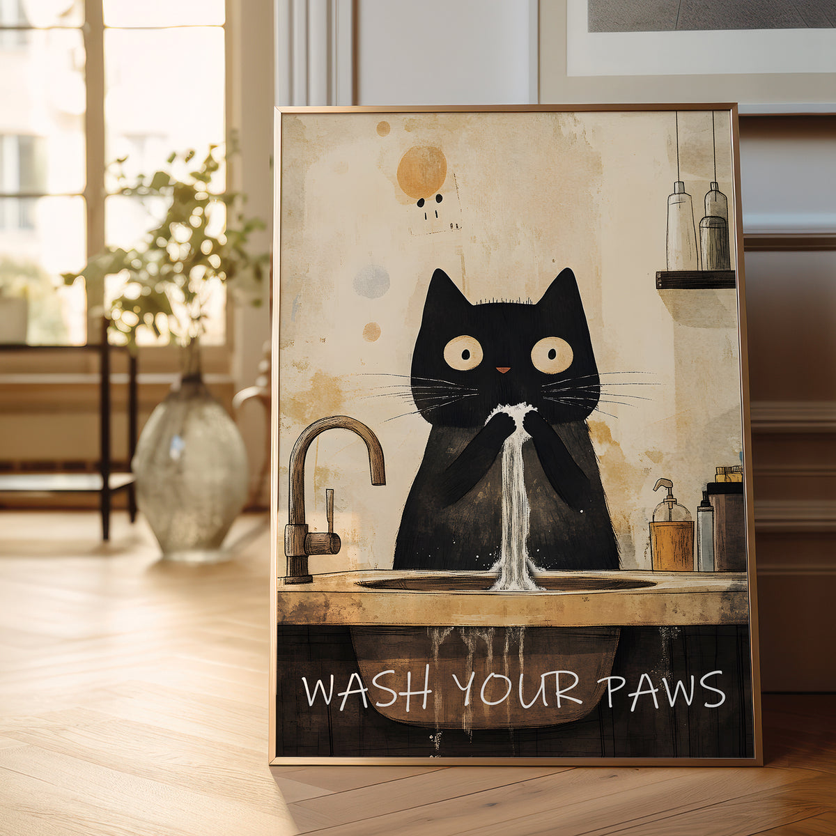 A framed art print featuring a black cat washing its paws at a sink, with the text 'WASH YOUR PAWS' at the bottom, displayed in a bright, modern room.