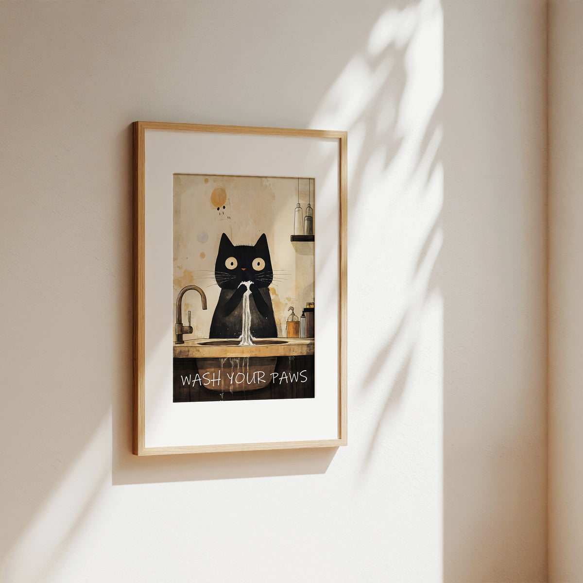A framed art print featuring a black cat washing its paws at a sink, hung on a warm beige wall with soft window shadows cast across it.
