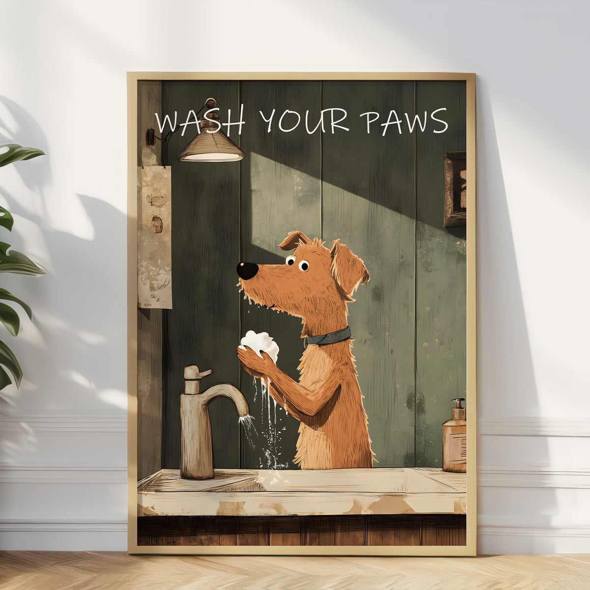 A framed art print leaning against a white wall on a light wood floor. The print shows an illustrated brown dog washing its paws at a sink, with the text 'WASH YOUR PAWS' at the top.