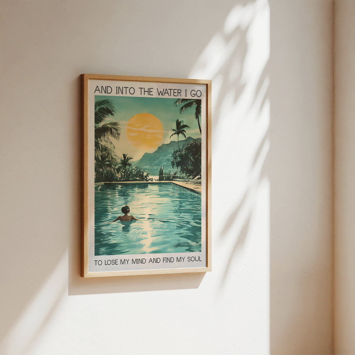 Framed poster of a pool scene with palm trees and a sunset, on a wall.