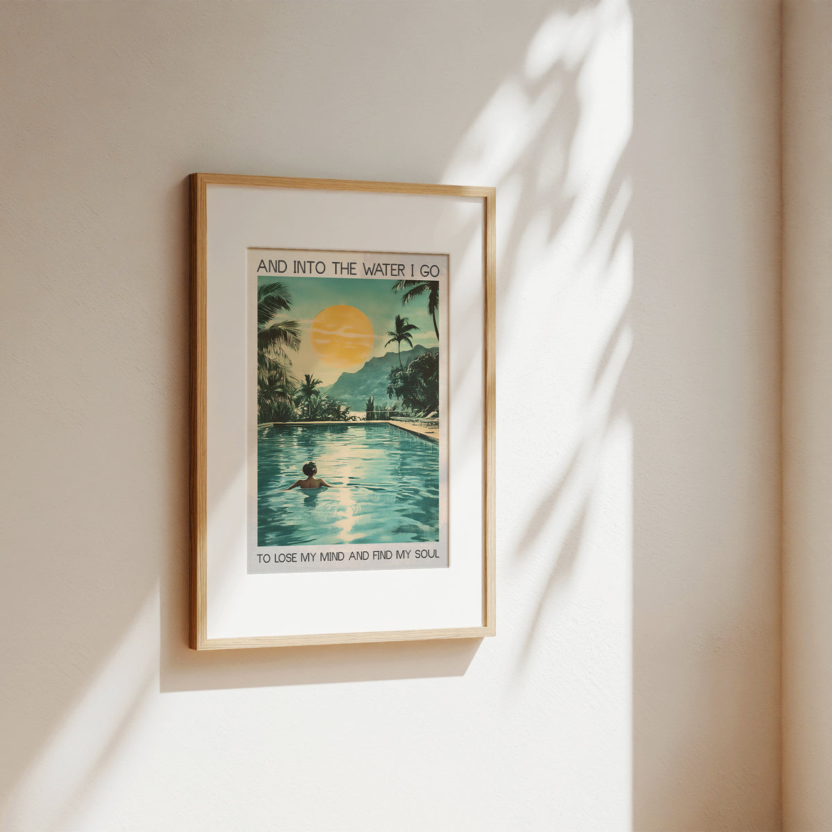 Framed artwork of a tropical scene with a pool and sunset, on a beige wall.