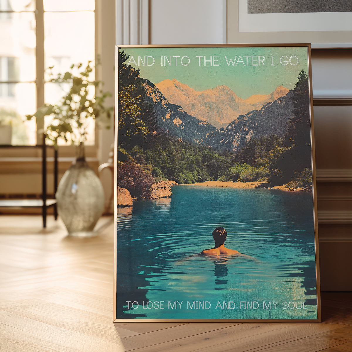 Framed poster of a person in a lake with mountains and text in a room with a plant and vase.