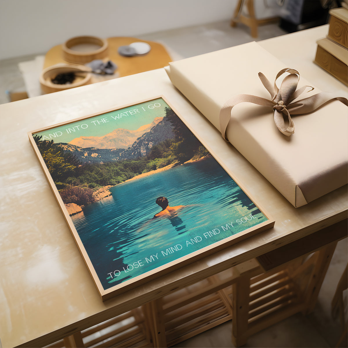 Poster of a person in a lake with mountains and a wrapped gift on a table.