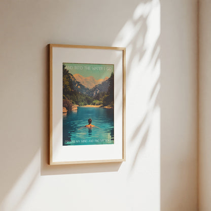 Framed poster of a mountain landscape with a person in water on a beige wall.