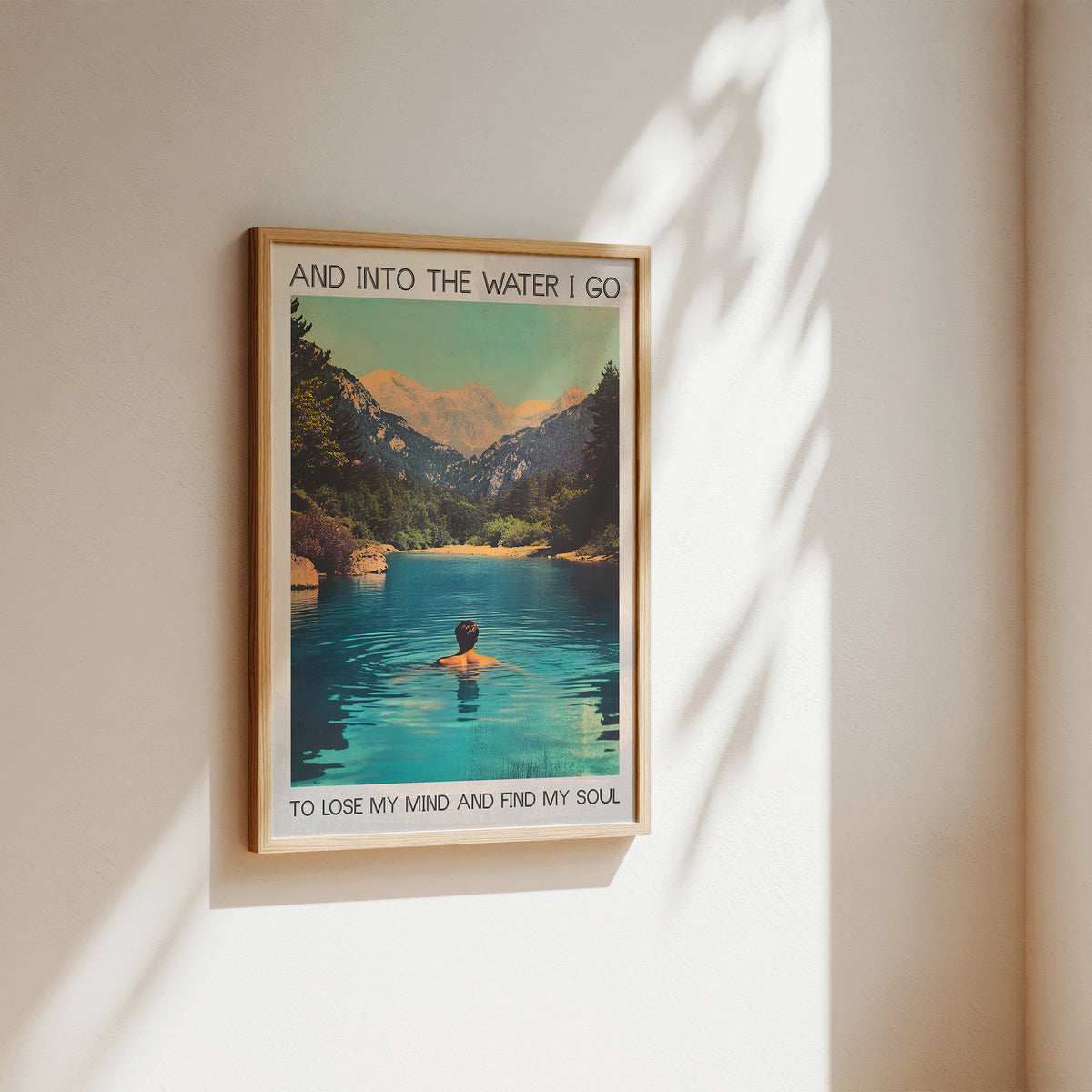 Framed poster of a person in a lake with mountains, text 'And into the water I go to lose my mind and find my soul', on a wall.