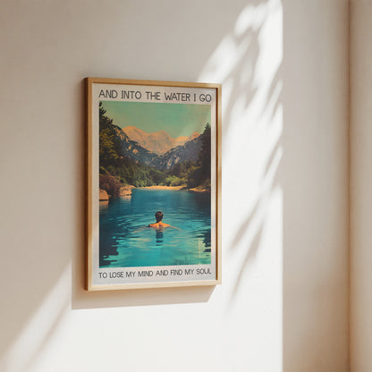Framed poster of a person in a lake with mountains, text 'And into the water I go to lose my mind and find my soul', on a wall.