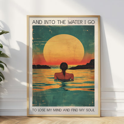 Framed artwork of a woman in water with a sunset, text 'And into the water I go / To lose my mind and find my soul', on a white wall.
